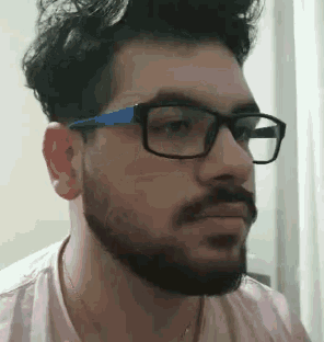 a man with a beard wearing glasses and a pink shirt is making a funny face .