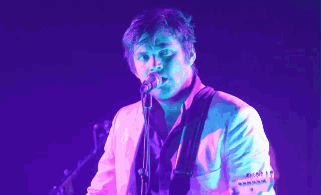 a man singing into a microphone while playing a guitar in front of a purple background