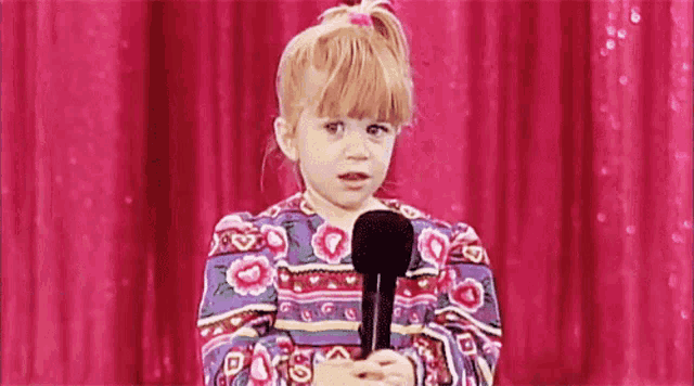 a little girl is holding a microphone and making a funny face .