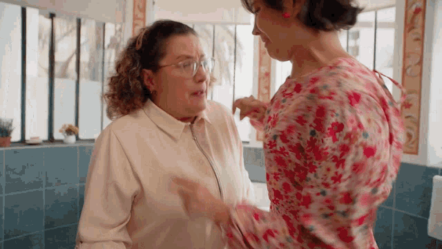 a woman in a floral shirt is talking to another woman in a white shirt