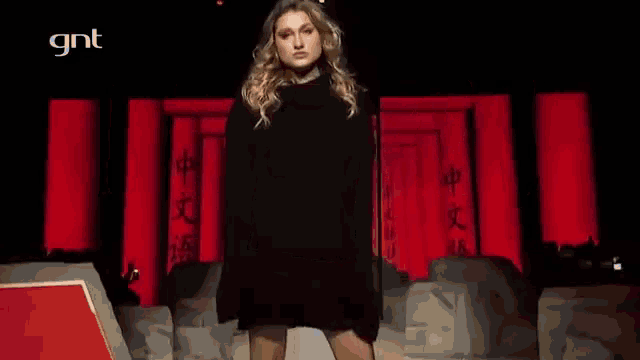 a woman in a black dress is walking down a runway with gnt written on the bottom