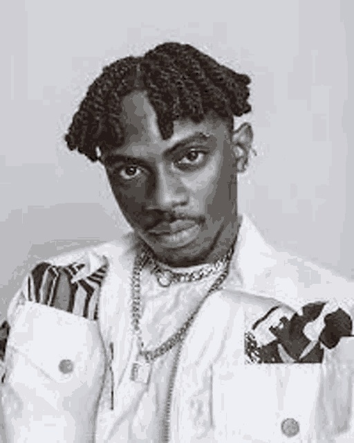 a black and white photo of a young man wearing a white jacket and a chain .