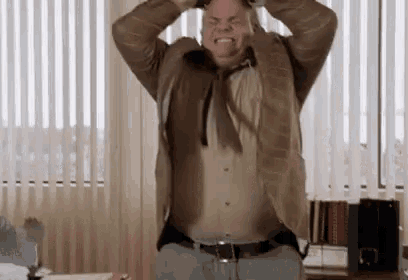 a man is standing in an office with his hands on his head and screaming .