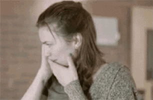 a woman is covering her mouth with her hands while sitting at a table in a kitchen .