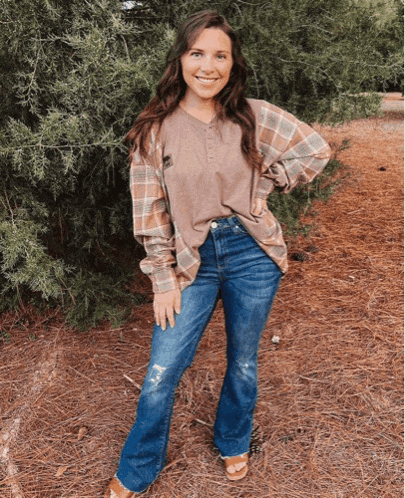 a woman wearing a plaid shirt and jeans is standing in the woods