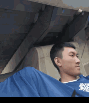 a man wearing a blue shirt with chinese writing on it is sitting on a plane