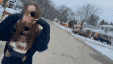 a woman wearing sunglasses and a sweater is walking down a snowy street