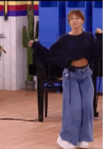 a woman in a black sweater and blue jeans is dancing on a dance floor .