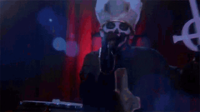 a man in a skull mask is singing into a microphone while holding a cross