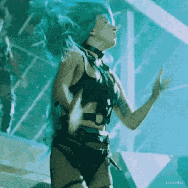 a woman with blue hair is dancing in front of a sign that says gohookery