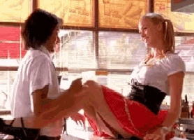 a woman in a red skirt is sitting on a man 's lap in front of a window .