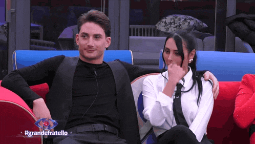 a man and a woman are sitting on a red couch with the hashtag grandefratello on the bottom