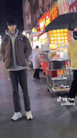 a man in a brown jacket stands in front of a food stand with chinese writing on it