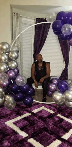 a man sits in front of a purple and silver balloon display