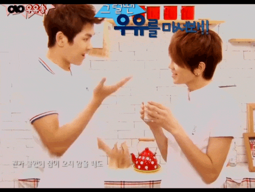 two young men are talking in front of a brick wall and a sign that says ' aoo ' on it