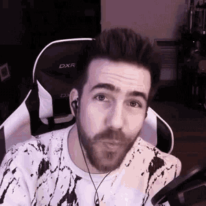 a man with a beard is sitting in a chair wearing headphones and making a funny face .