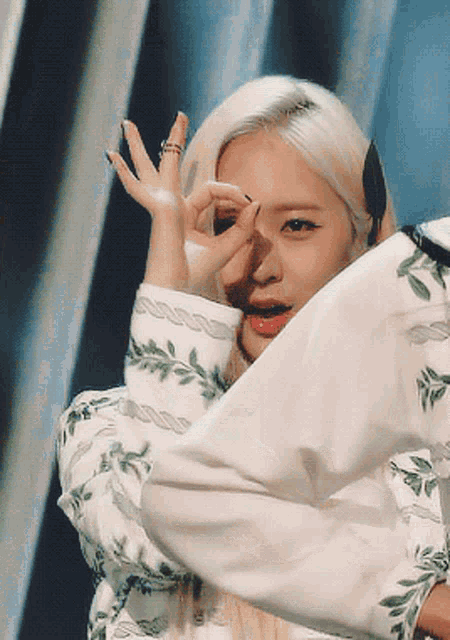 a woman with blonde hair and green leaves on her sleeves is making a peace sign