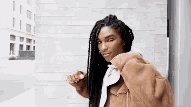 a woman with long braids is standing in front of a brick wall .