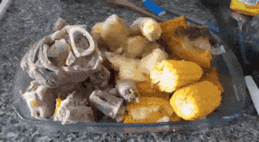a casserole dish filled with corn on the cob potatoes and bones