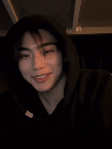 a man wearing a black hoodie is smiling and covering his mouth