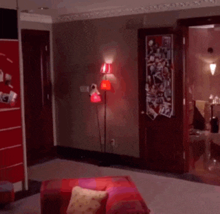 a woman walking through a living room with a red lamp