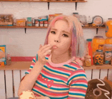 a woman with colorful hair is eating a donut in a kitchen .