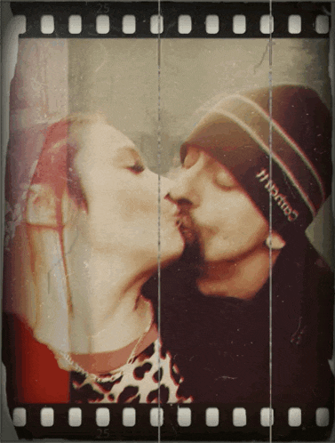 a man wearing a hat that says hanes kisses a woman on the cheek