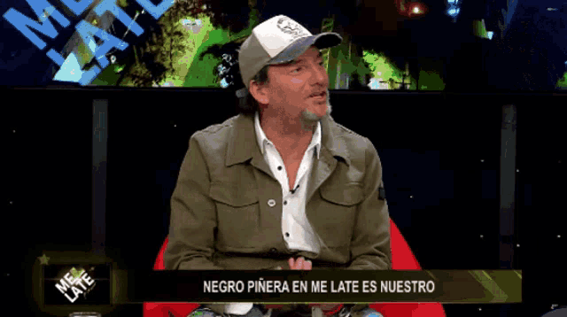 a man wearing a hat is sitting in front of a sign that says negro pinera en me late es nuestro