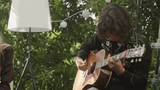 a man is playing an acoustic guitar in front of trees