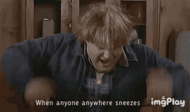 a man is sneezing in front of a wooden cabinet .