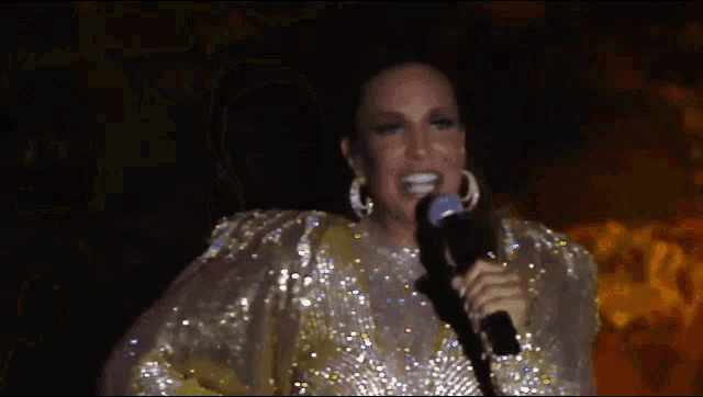a woman in a gold sequined dress is holding a microphone .