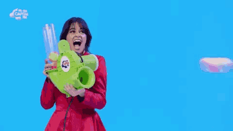 a woman in a red dress is holding a green water gun that says capital fm