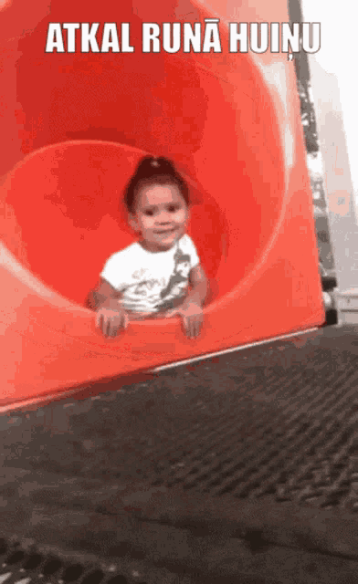 a little girl is sitting on a slide with the words atkal runa huinu written above her
