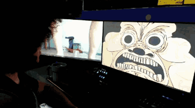 a person sitting in front of two computer monitors one of which has a cartoon on it