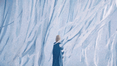 a woman in a blue coat stands in front of a wall of white papers