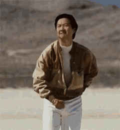 a man in a brown jacket and white pants is standing in a desert
