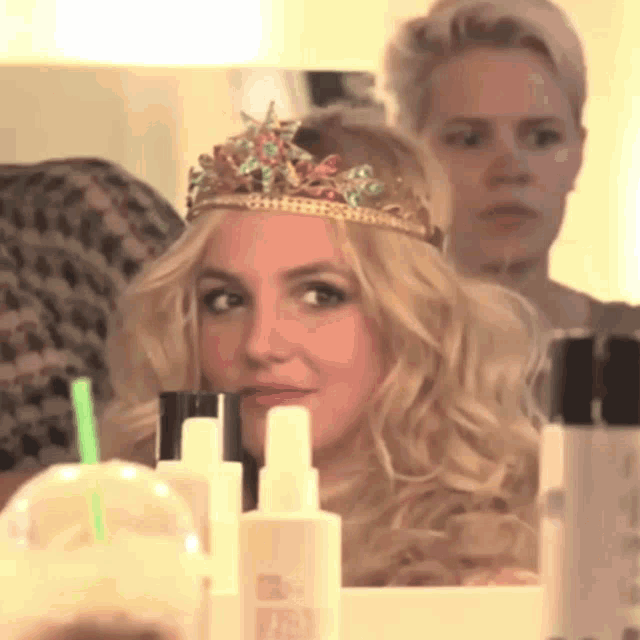 a woman with a crown on her head looks at herself in a mirror