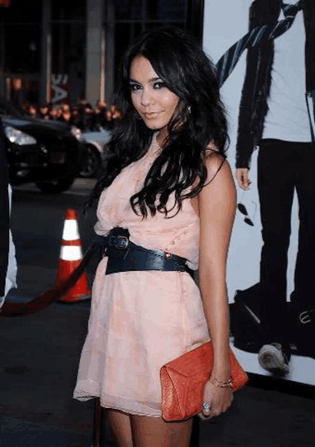 a woman in a pink dress is holding a red clutch and wearing a black belt .