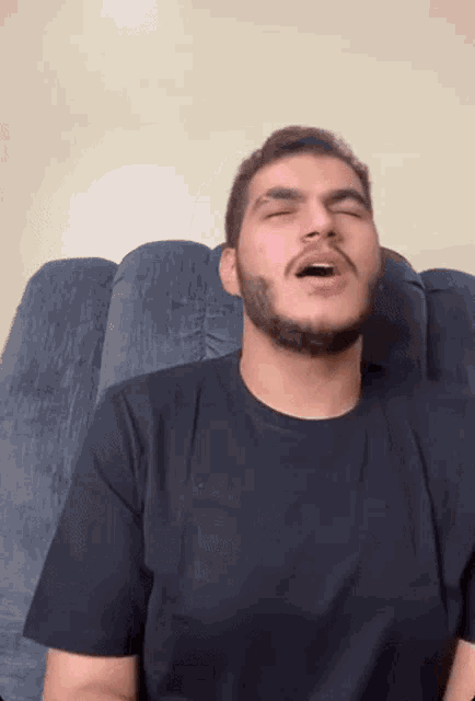 a man with a beard is yawning while sitting in a chair .