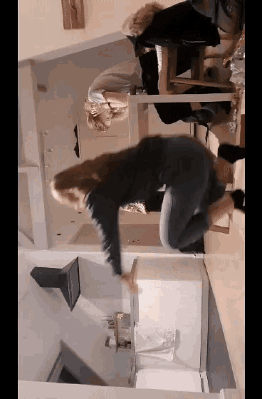 a woman is jumping in the air in a kitchen while a man sits at a table