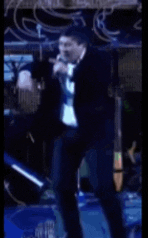 a man in a suit is dancing on stage in front of a drum set