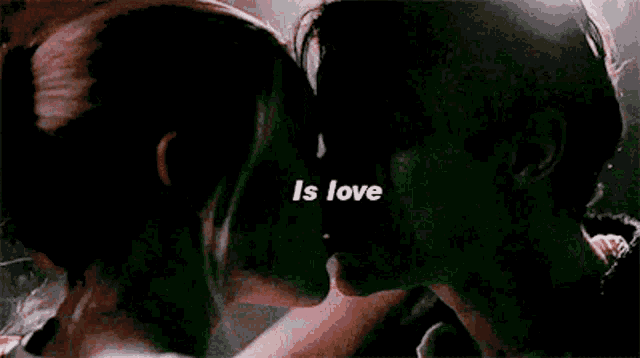 a man and a woman are kissing in a dark room with the words `` is love '' above them .