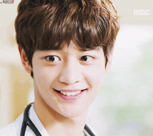 a young man with a stethoscope around his neck smiles for the camera with a mbc logo behind him
