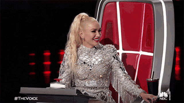 a woman in a silver dress is sitting in a chair with a nbc logo