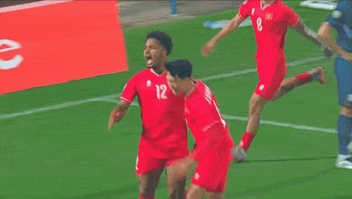 a soccer player with the number 12 on his jersey is surrounded by his teammates