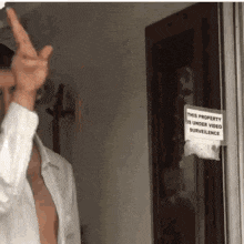 a man in a white shirt is giving the middle finger in front of a sign that says this property is under video surveillance .