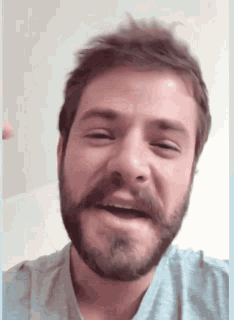 a man with a beard is smiling and wearing a light blue shirt