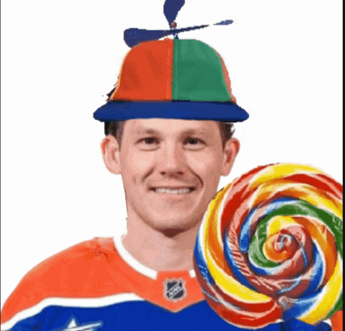 a man wearing a hat with a propeller is holding a large lollipop