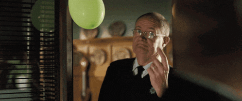 a man looking at himself in the mirror with a green balloon behind him