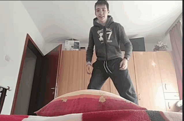 a boy wearing a hoodie with the number 7 on it is jumping on a bed